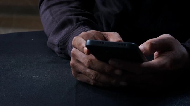 Phone scammers, unrecognizable man holding a smartphone, anonymous cyber criminal performing phishing attack, identity theft via mobile phone, threat to privacy and digital security.