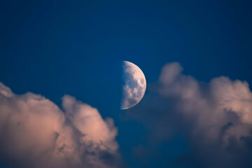 Obraz premium A serene night sky with a half moon shining through soft, fluffy clouds