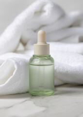 Closed green glass dropper bottle near white bath towel, skincare serum packaging mockup