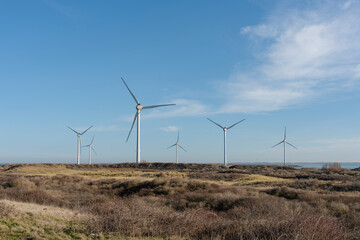 Wind turbines against a light blue sky in a barren landscape.