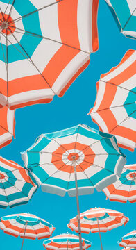 Looking up at striped parasol against azure sky, creating vibrant geometric pattern, representing summer vacation, sun protection, or beach atmosphere