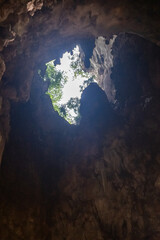Upward view from inside Batu Caves near Kuala Lumpur, Malaysia. Showing a natural opening in the limestone cave with sunlight and greenery.