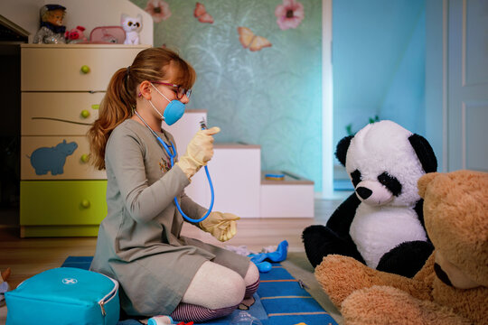Little girl playing doctor role game with her plush toys at home.
