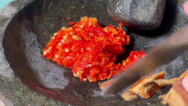 Making traditional spicy sambal chili paste using a stone mortar and pestle.
