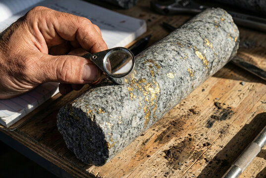 Geologist Examining Gold Veins in Rock Core Sample with Magnifying Glass; Mineral Exploration and Mining Geology Concept.