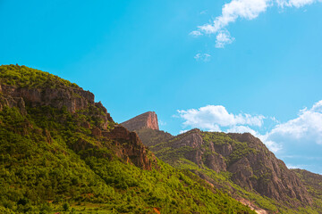 Lush green mountains covered with forest under a clear blue sky with clouds. Showcasing natural beauty, wilderness, outdoor travel, peaceful environment and scenic landscape background.