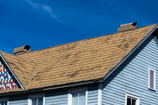 An old damaged shingles roof on a blue sky