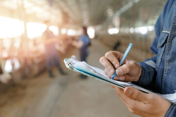 Person writing on clipboard in agricultural setting with blurred workers in background