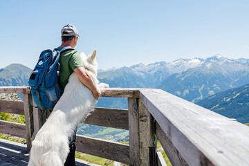 Obraz premium Hiker embracing white swiss shepherd dog enjoying mountain view from wooden terrace