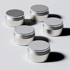 Row of five small jars with lids sit on a white background. The jars are all the same color and have a silver lid. The jars are arranged in a neat row, with the first jar on the left