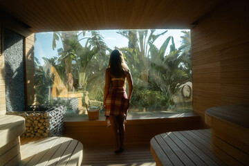 Sauna Escape: A person walks towards a panoramic window in a sauna, overlooking a lush tropical landscape, creating a sense of serene escape and tranquility.