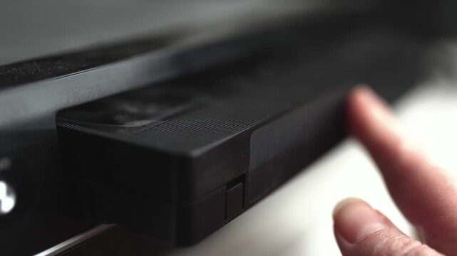 Close up of a hand holding a videotape. Retro vhs cassete in a player.	