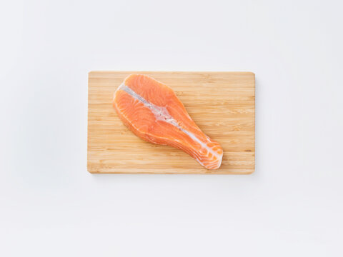 A salmon fillet sits on a wooden cutting board. The fillet has a bright orange color and is prepared for cooking. It is placed in a clean kitchen setting with a simple background