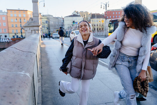 Laughing teenage girl walking with confident smiling woman on city bridge