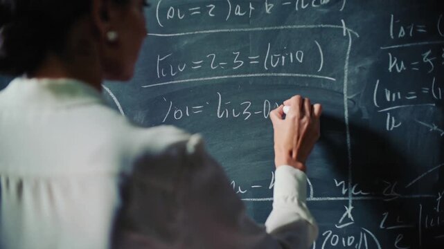 Mathematics professor writing complex equations on large chalkboard in vintage classroom. Panning shot moving into close-up.