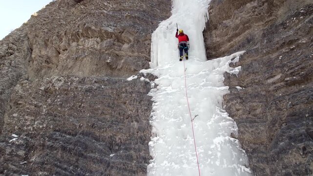 a mountaineer ice climbing on a frozen waterfall.