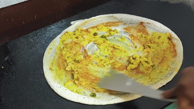 Close-up of masala dosa cooking on a flat iron griddle. Crispy texture and motion highlight traditional South Indian street food preparation.