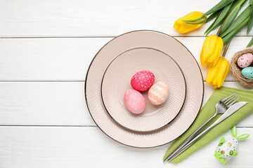 Easter celebration. Festive setting with cutlery, flowers and painted eggs on white wooden table, flat lay. Space for text