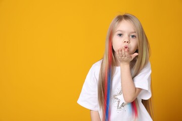 Cute girl with colorful clip-in hair extensions sending air kiss on yellow background. Space for text
