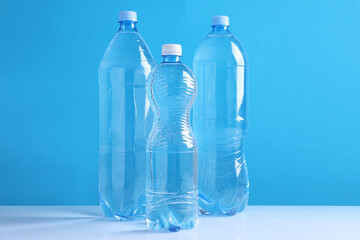 Fototapeta premium Bottles of fresh water on white table against light blue background