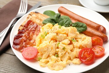 Tasty breakfast. Delicious scrambled eggs with bacon, sausages and tomatoes served on table, closeup