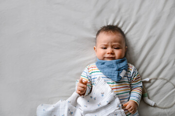 Fototapeta premium A baby is laying on a bed with a blue bandana around its neck.