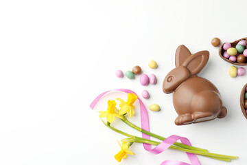 Obraz premium Chocolate Easter bunny, flowers, ribbon and eggs on white background, flat lay. Space for text