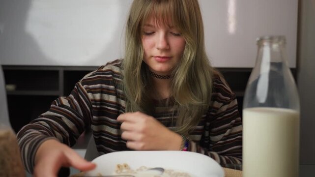 Playful teenager girl with green hair amusingly waiting for breakfast to be ready, clapping hands with impatience before finally enjoy bowl of cereal with milk at home