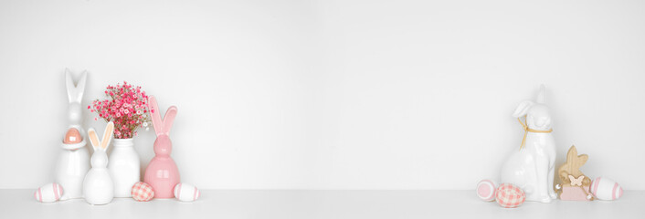 Naklejka premium Easter decor on a white shelf. Easter bunnies, flowers, eggs against a white wall banner background. Copy space.