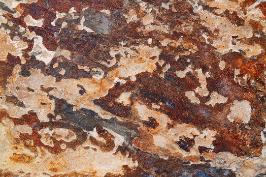 Rough, earthy surface of weathered flagstone or rock with natural cracks and a striking color gradient of terracotta and rust.