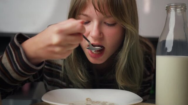 Teenage girl eating cereal at the kitchen table. Domestic life scene, cozy home morning, simple food, real family routine and everyday lifestyle concept.