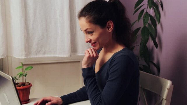 Happy business woman working at the laptop with emotional beauty face sitting at the table. Female looking in the screen of notebook