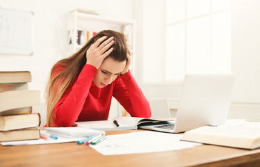 A young woman in a red sweater sits at a cluttered desk, feeling overwhelmed while studying. Books...