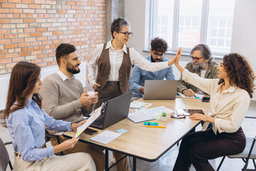 Fototapeta premium Diverse business team collaborating and celebrating success with high five gesture during office meeting