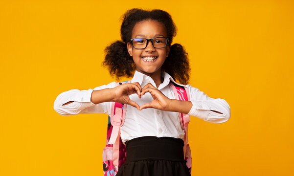 Adorable African American Schoolgirl Showing Heart Gesture With Hands Over Yellow Background In Studio. Love School Concept