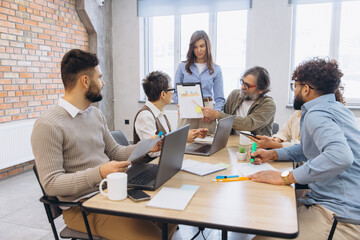 Obraz premium Diverse business team collaborating during a meeting, discussing financial data with a presentation board in a modern office
