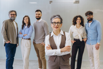Obraz premium Mature woman leading a diverse business team smiling in a modern office workplace, showing teamwork and success