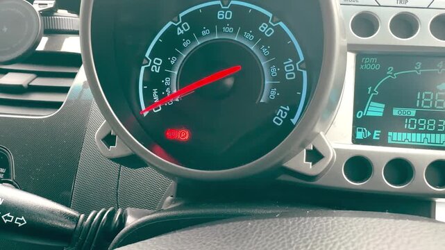 Close up of a car speedometer with red warning icons for seatbelt and parking brake