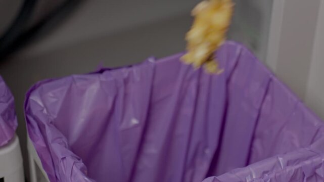 Close up of hand dropping apple core into trash bin in kitchen. Concept of food waste disposal and household hygiene