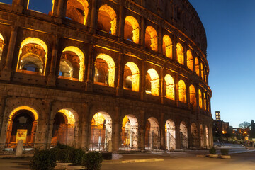 Evening cityscape with ancient walls of Colosseum in Rome, Italy. Texture of weathered travertine stone and Roman brickwork under blue sky.