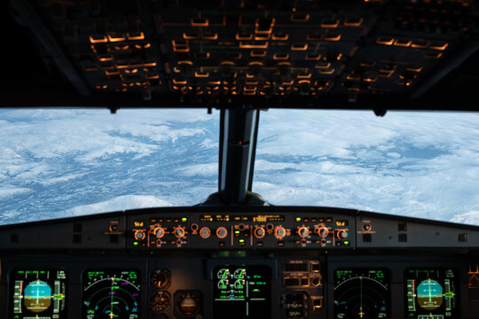 Airplane cockpit flying over snow-covered mountains