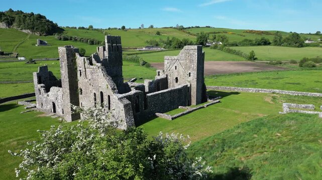 Cinematic drone footage featuring a vertical rise up flight revealing the ancient ruins of Fore Abbey in County Westmeath, Ireland. The shot captures the historic Benedictine priory surrounded by lush