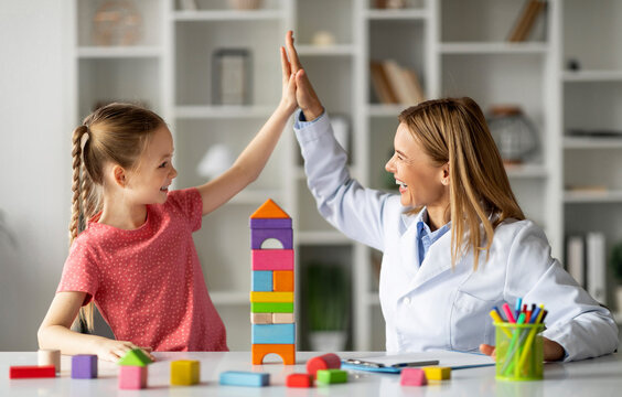 Cute Little Girl Giving High Five To Child Development Specialist During Meeting In Office, Smiling Therapist Lady Greeting Happy Kid With Progress, Celebrating Successful Therapy