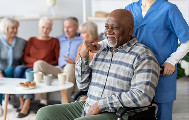 Naklejka premium Disabled african american senior man in wheelchair holding nurse hand, looking at copy space and smiling, thanking for support, life in nursing home for elderly people concept