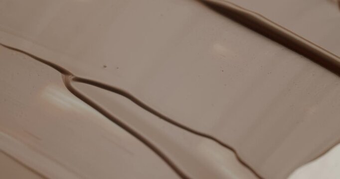 Extreme close-up of a cosmetic spatula smearing a creamy makeup foundation, creating beautiful textures and strokes in a satisfying, slow-motion cosmetic laboratory demonstration