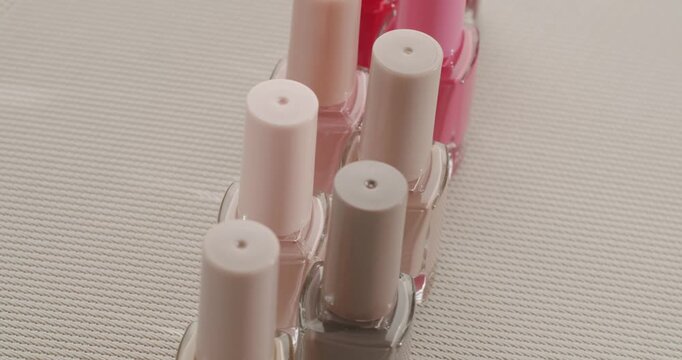 Rows of colorful nail polish bottles with various shades of pink, red, and nude on a textured surface. Manicure and pedicure concept with a large palette of cosmetic varnish for beauty care