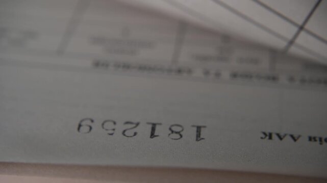 Close-up video footage of automatic page numbering process. A mechanical numbering device places a unique serial number on each page one by one