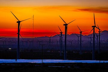 Fototapeta premium Scenic crimson panoramic sunset in California with multiple wind energy turbines silhouettes