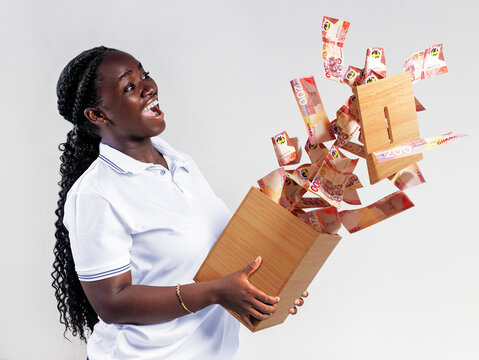 A joyful woman holds a wooden savings box as Ghanaian 200 Cedi notes erupt upward. Her ecstatic expression captures financial freedom, successful saving, and the excitement of hitting a money goal