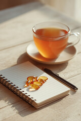 Cup of herbal tea with dietary supplement capsules on minimalist wooden desk. Wellness lifestyle, self care, healthy habits, and modern holistic concept.